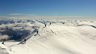 Bergsteiger auf schneebedecktem Gipfel mit Bergpanorama und Wolken