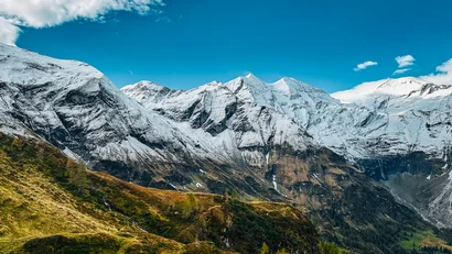 Schneebedeckte Berge unter blauem Himmel mit grüner Wiese im Vordergrund