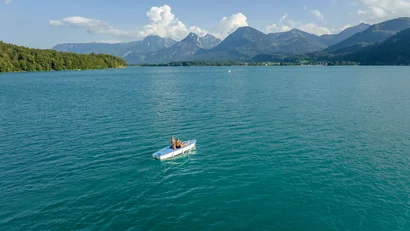 Blick auf ein Boot mit Menschen auf einem See vor Bergen und bewölktem Himmel