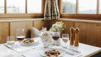 Gedeckter Tisch mit Essen, Weingläsern und Blumendekoration in einem Holzraum