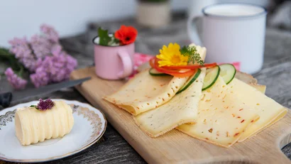 Verschiedene Käsesorten auf Holzbrett mit Butter und Milch im Hintergrund.