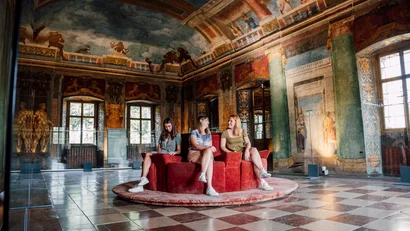 Drei Frauen sitzen auf rotem Sofa in einem kunstvoll bemalten historischen Raum