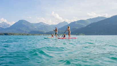 Familie paddelt auf Stand-Up-Paddle-Boards auf einem See mit Bergblick