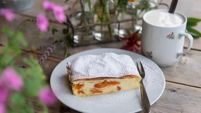 Kuchen mit Puderzucker auf weißem Teller neben Tasse mit Getränk