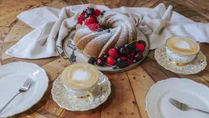 Gugelhupf mit Puderzucker und Beeren mit zwei Cappuccinos auf Holztisch