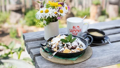 Kaiserschmarrn mit Puderzucker, Sauce, Becher und Blumenvase auf Holztisch