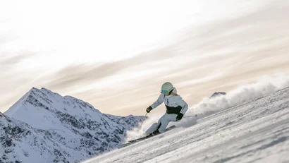 Skifahrerin fährt eine schneebedeckte Piste mit Bergen im Hintergrund hinunter