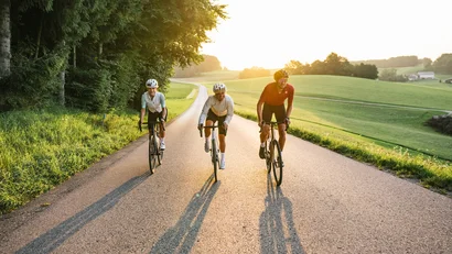 Drei Radfahrer fahren auf einer Landstraße bei Sonnenschein
