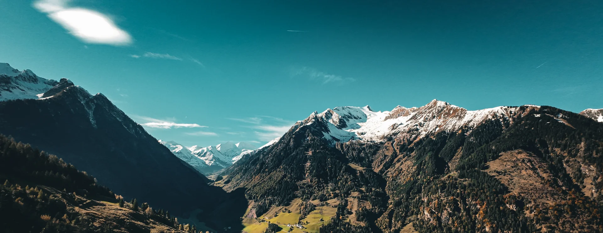 Bergtal mit schneebedeckten Gipfeln und grünem Talboden bei klarem Himmel