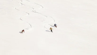 Drei Skifahrer fahren eine verschneite Piste hinunter mit frischen Spuren